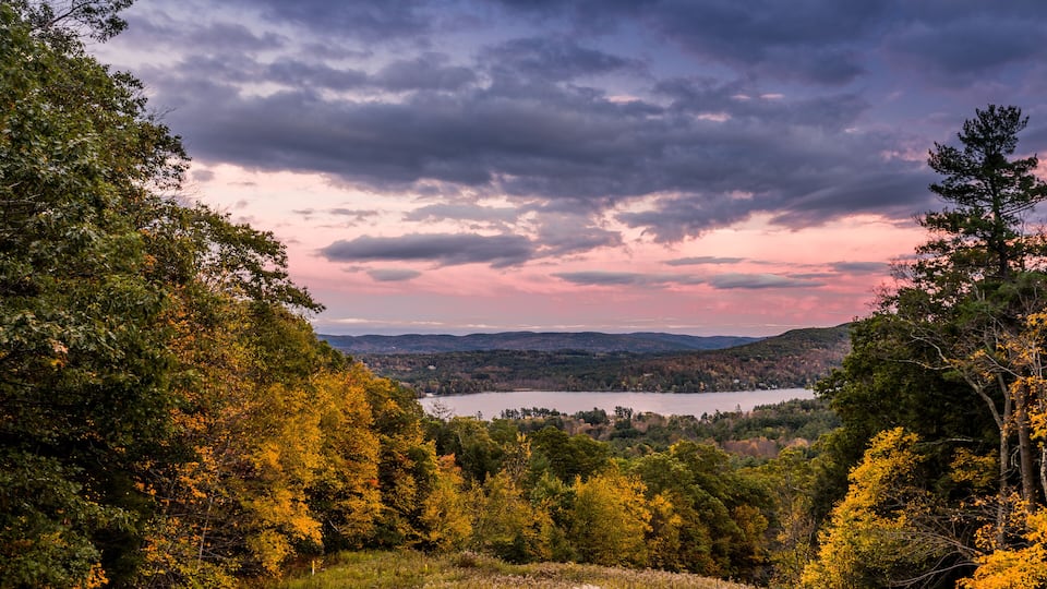 A lake surrounded by autumn-colored trees and hills under a cloudy sky.