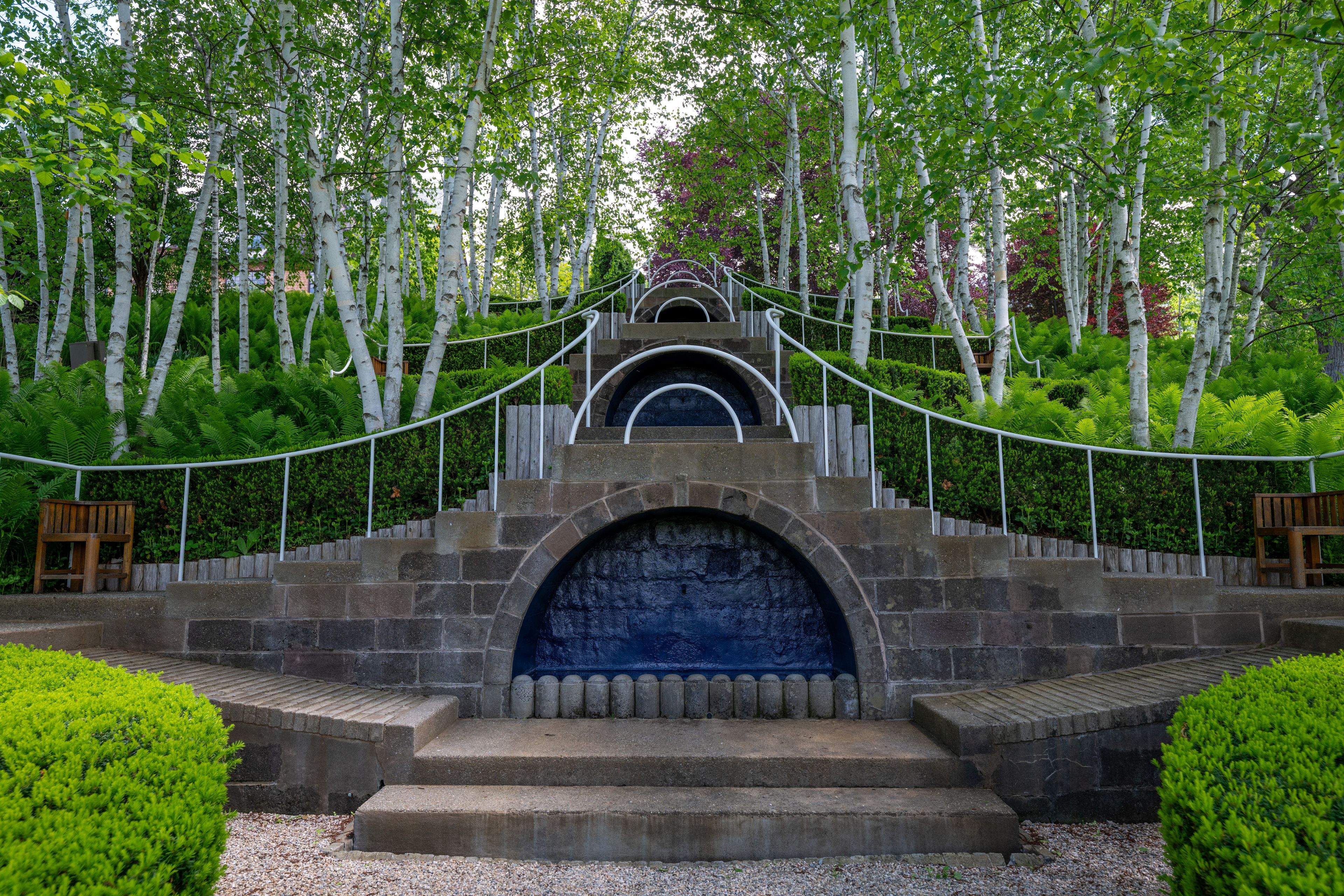 Una escalera de piedra conduce a una entrada azul con arco, rodeada de exuberante vegetación y abedules.