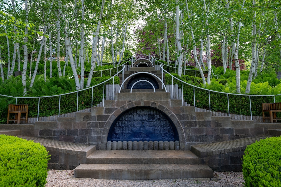 Una escalera de piedra conduce a una entrada azul con arco, rodeada de exuberante vegetación y abedules.