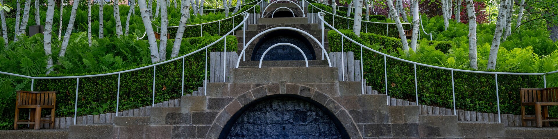 Una escalera de piedra conduce a una entrada azul con arco, rodeada de exuberante vegetación y abedules.