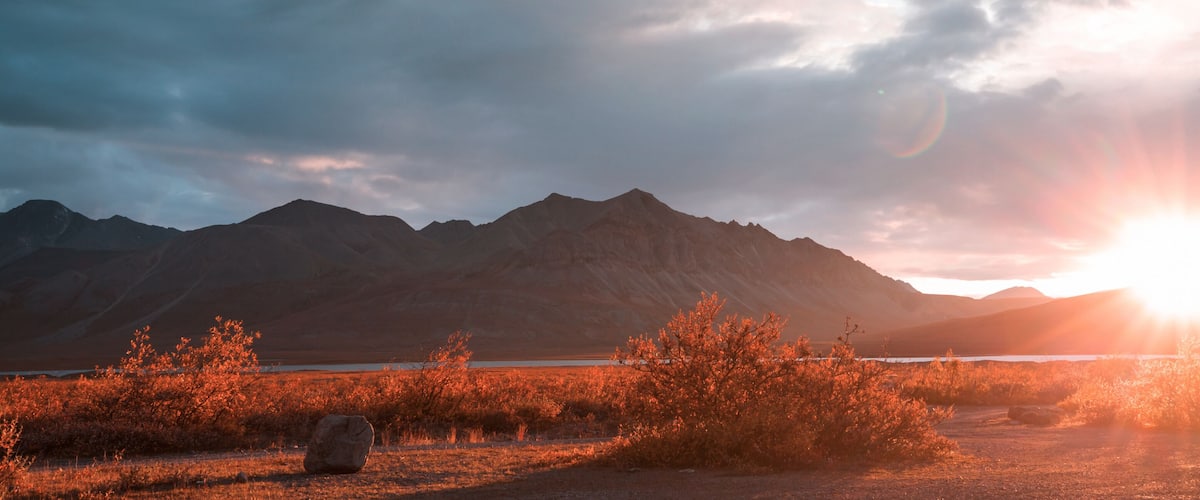 A sunset over a mountainous landscape with a body of water in the foreground.