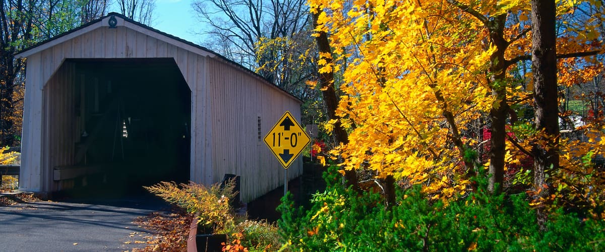 A covered bridge with a height restriction sign, surrounded by autumn foliage.