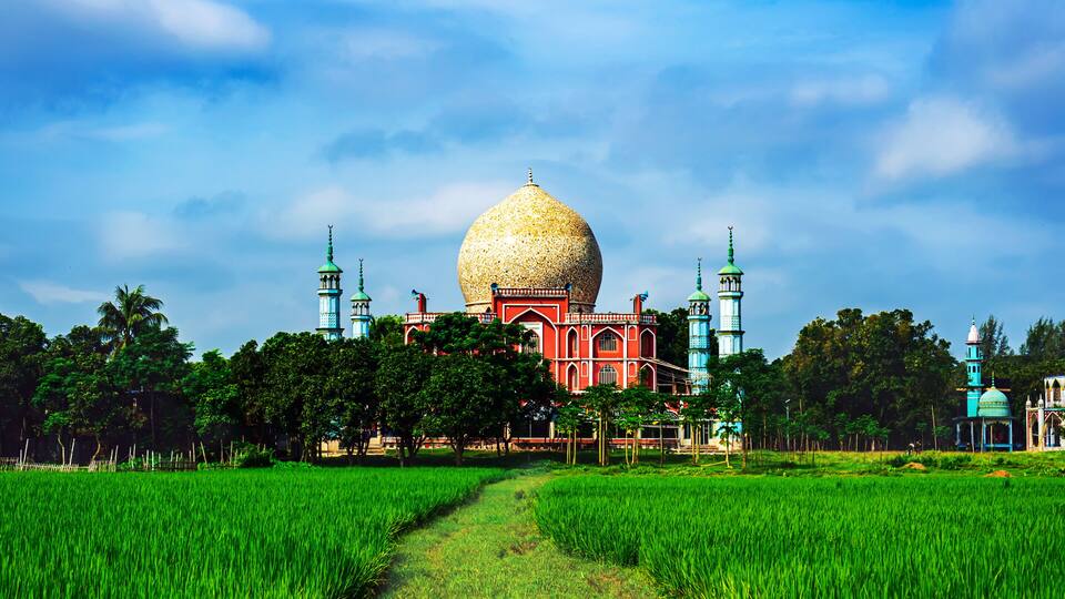 A large mosque with a golden dome and minarets, surrounded by lush green fields and trees.