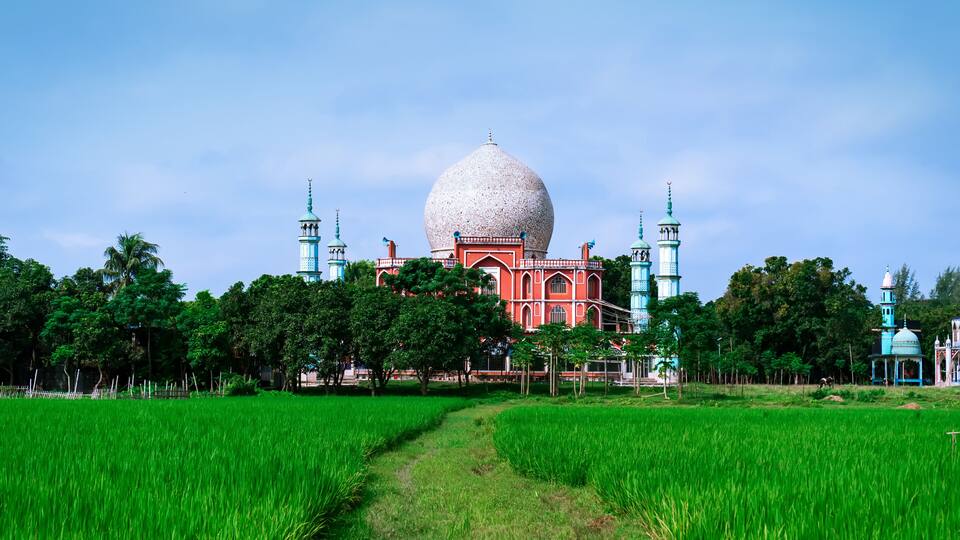 A mosque with a large dome and minarets, surrounded by lush green fields.