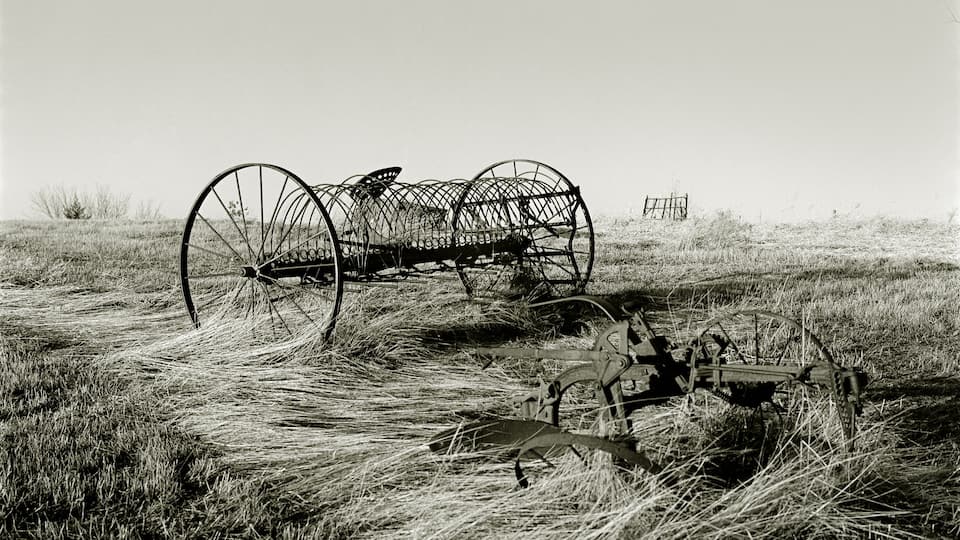 A vintage tractor and a wireframe structure in a grassy field.