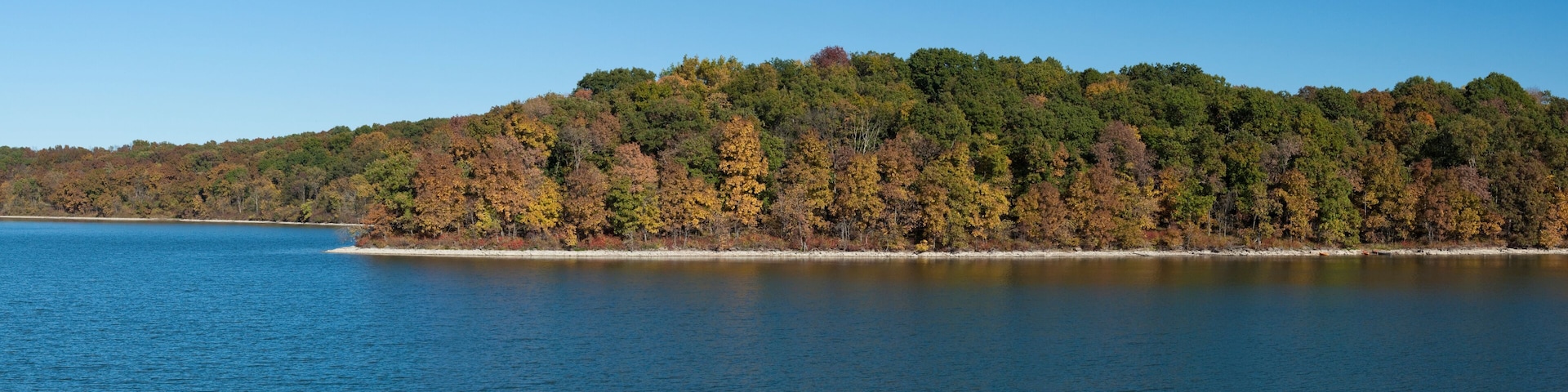 A calm lake with a forested island in the distance.