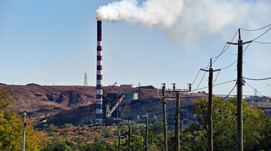 Industry town with mining chimney bellowing white smoke against blue sky.