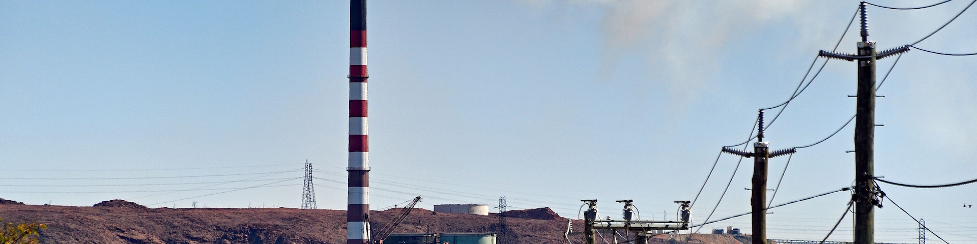Industry town with mining chimney bellowing white smoke against blue sky.