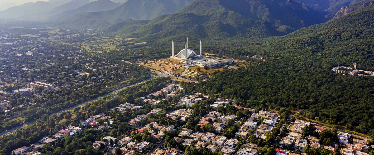 Une mosquée dotée d’un grand dôme et de minarets, entourée d’un quartier résidentiel densément peuplé et avec des montagnes en arrière-plan.