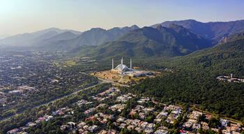 Une mosquée dotée d’un grand dôme et de minarets, entourée d’un quartier résidentiel densément peuplé et avec des montagnes en arrière-plan.