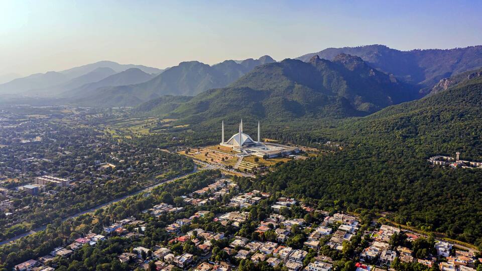 Eine Moschee mit einer großen Kuppel und Minaretten, umgeben von einem dicht bebauten Wohngebiet und Bergen im Hintergrund.