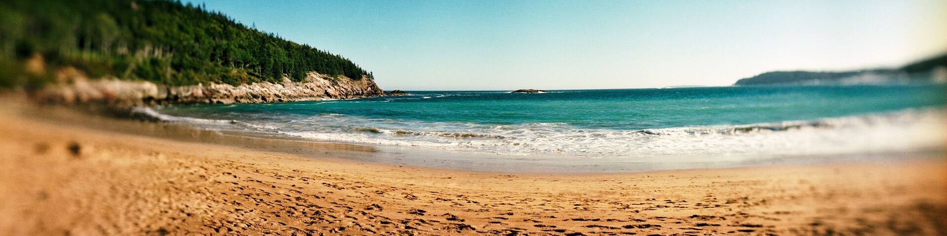 A beach with a forested cliff and calm sea.