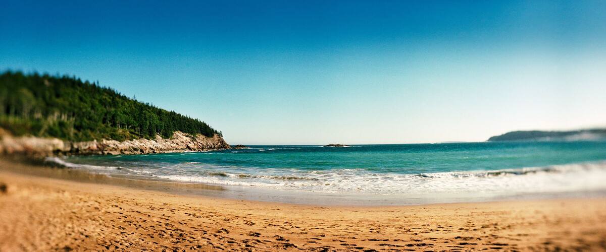 A beach with a forested cliff and calm sea.