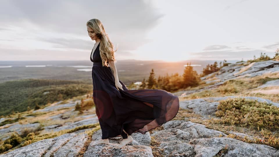 A person standing on a rocky outcrop with a vast landscape in the background.