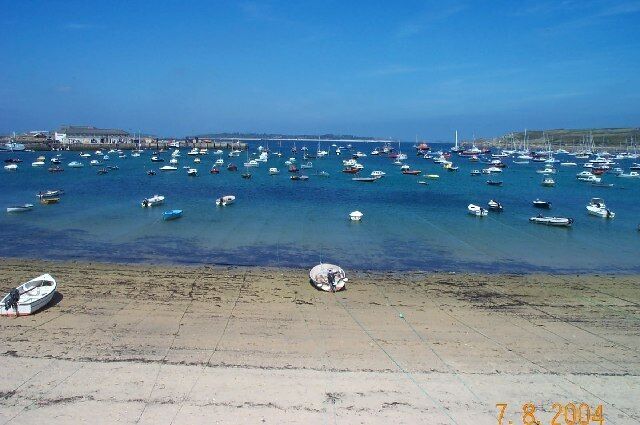 Escena costera con numerosos barcos anclados en el agua, una playa de arena y un puente a lo lejos.