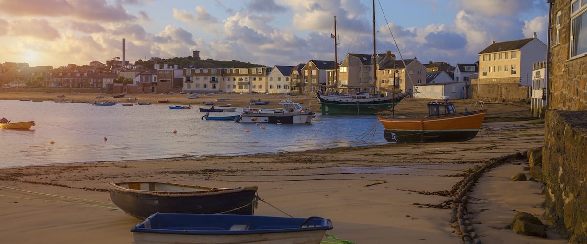 A coastal village with boats on the beach, a lighthouse, and houses along the shore.