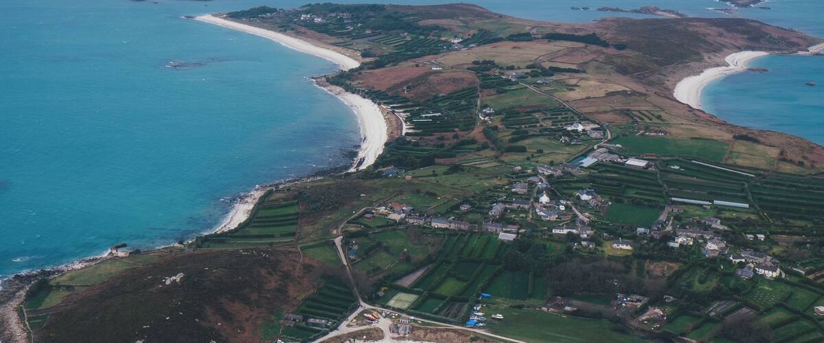 An aerial view of a coastal area with sandy beaches, green fields, and rocky outcrops.