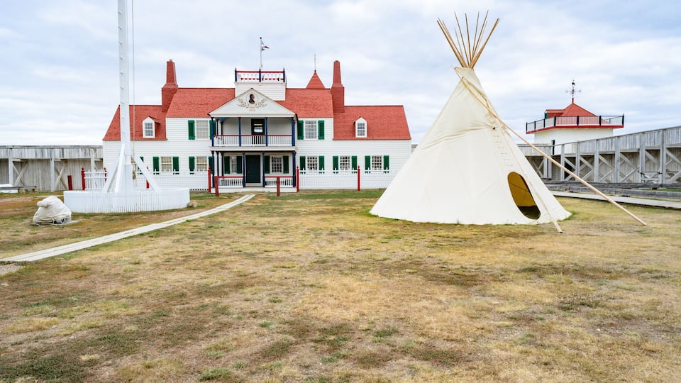 A white teepee, a white building with green shutters, and a red-roofed structure.