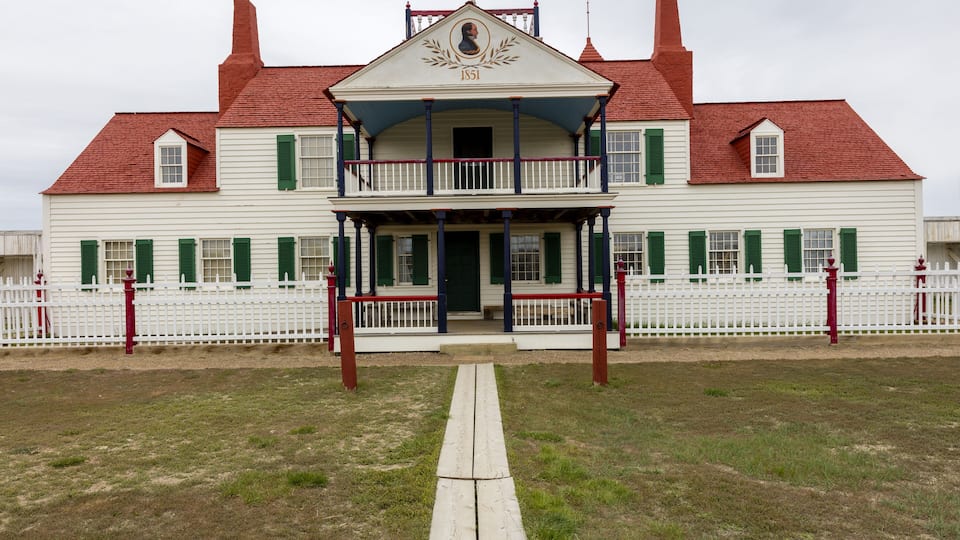 A white building with green shutters and a red roof, featuring a balcony and a year marker of 1851.