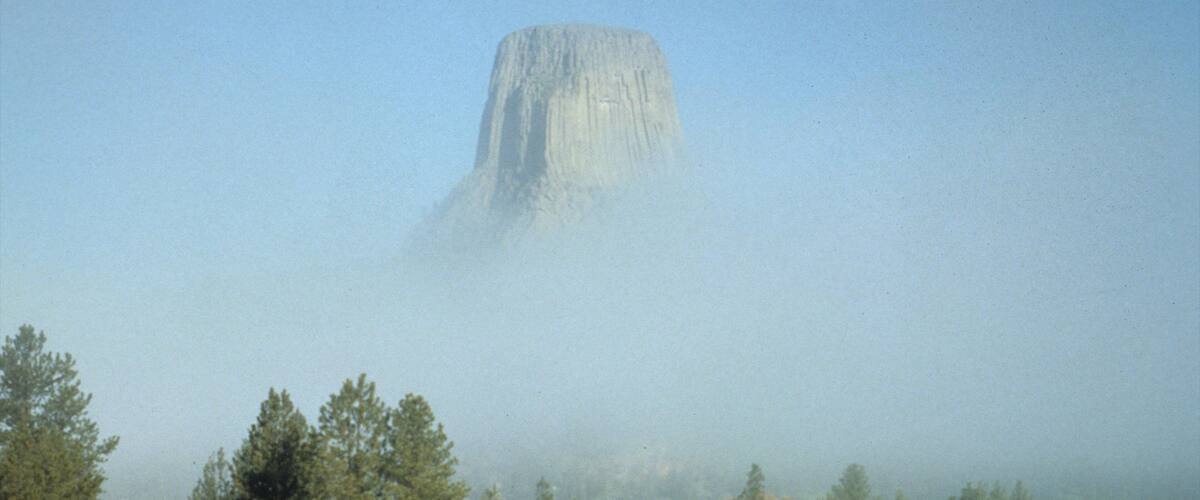 A large rock formation surrounded by trees and a grassy field.