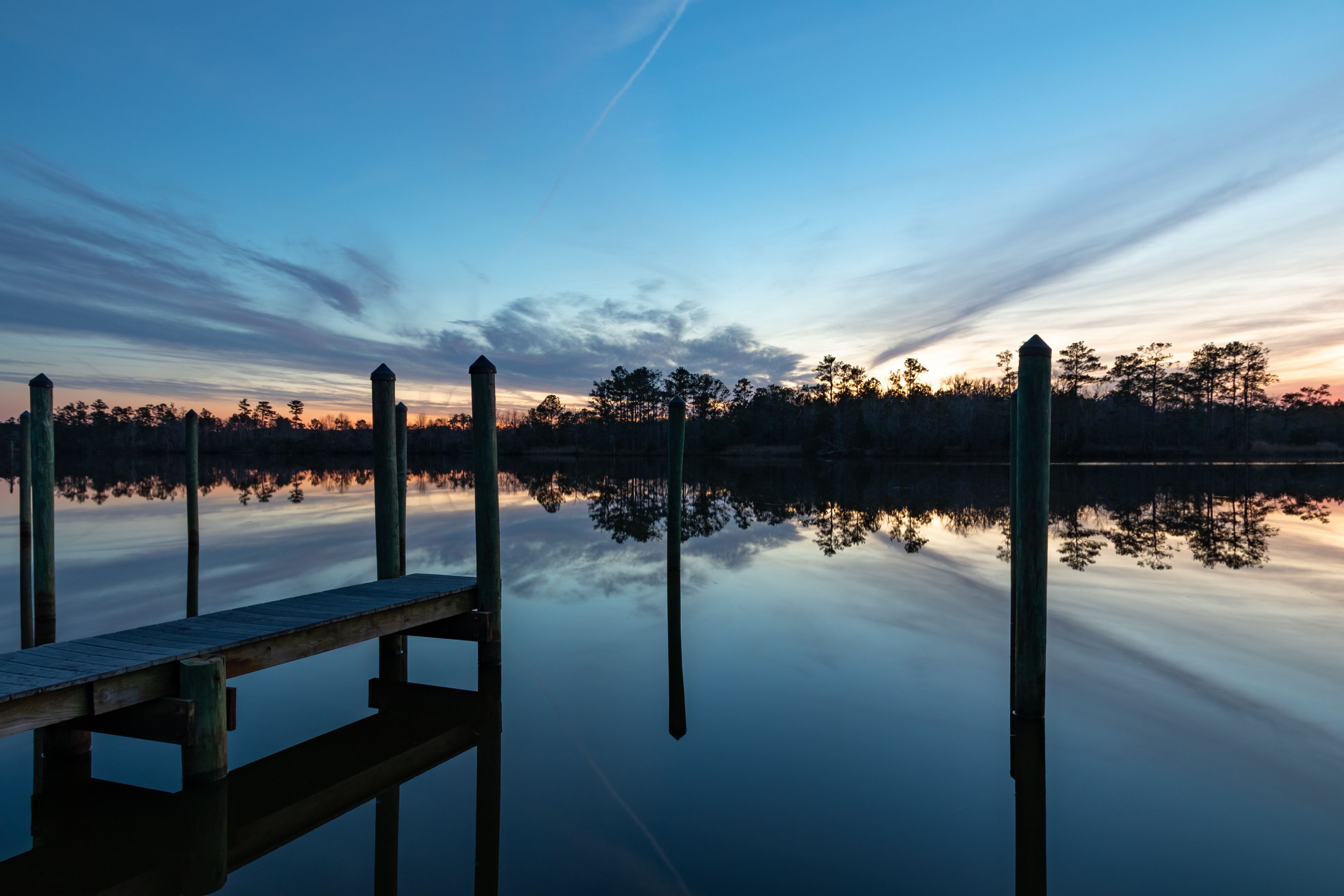 A wooden dock extending into calm water with a sunset in the background.