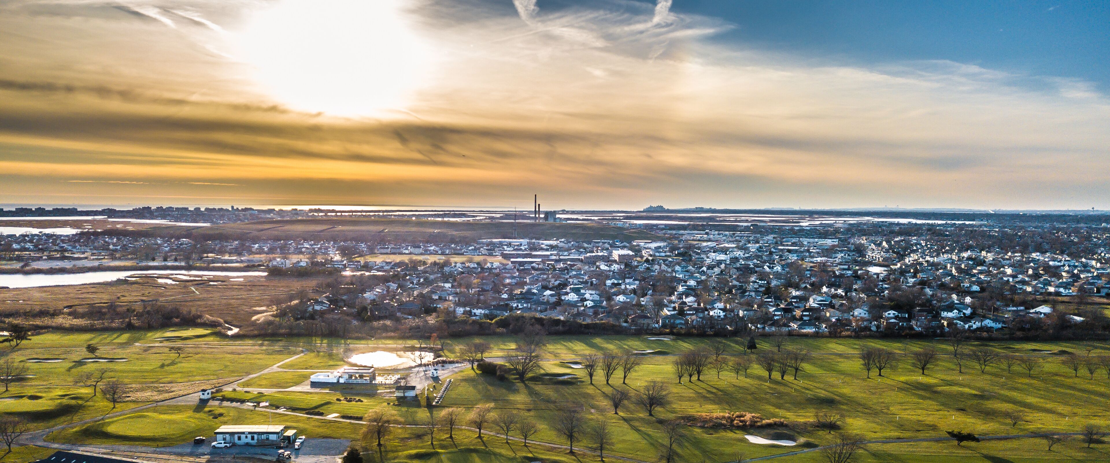 A cityscape with a large body of water, a bridge, and a golf course.