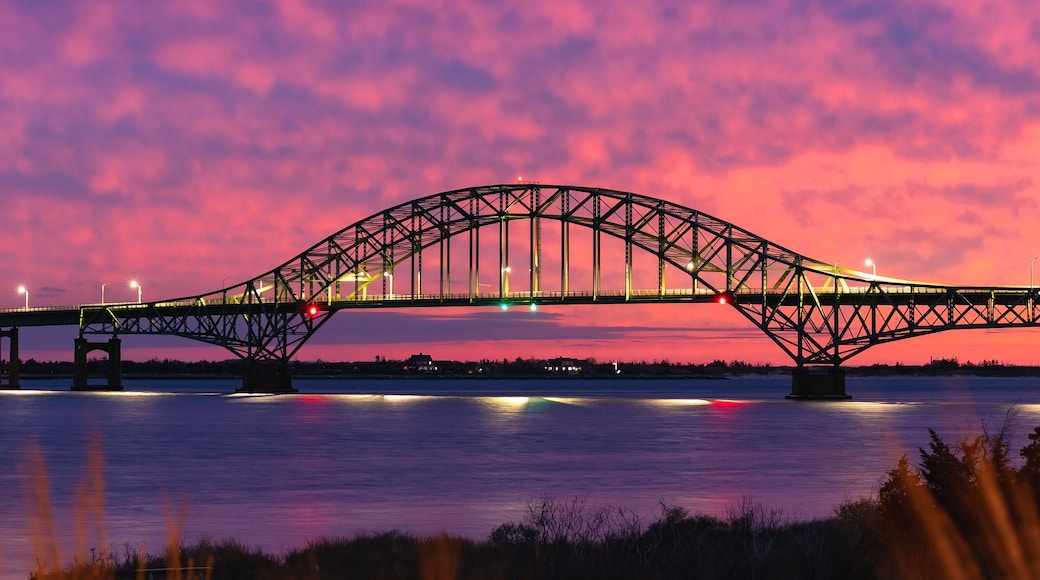 Vibrant colorful sunset sky behind a long steel tied arch bridge. Fire Island Inlet Bridge, Captree State Park New York