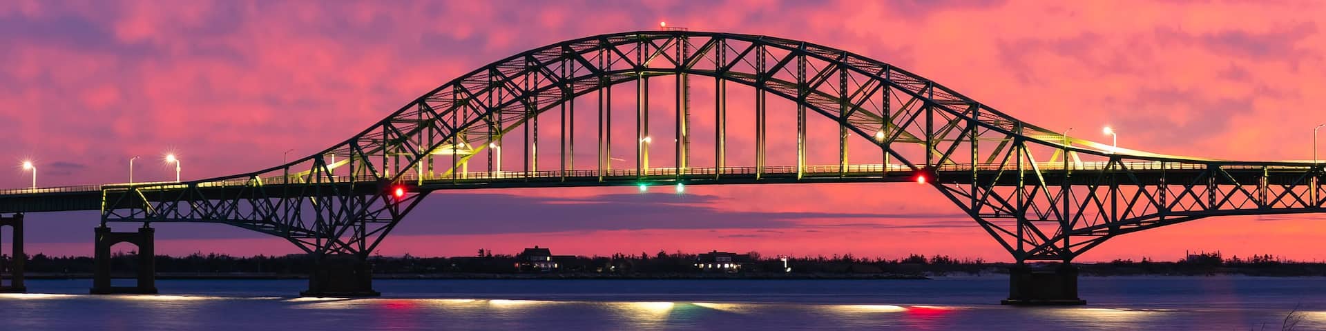 Vibrant colorful sunset sky behind a long steel tied arch bridge. Fire Island Inlet Bridge, Captree State Park New York