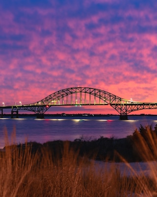 Vibrant colorful sunset sky behind a long steel tied arch bridge. Fire Island Inlet Bridge, Captree State Park New York