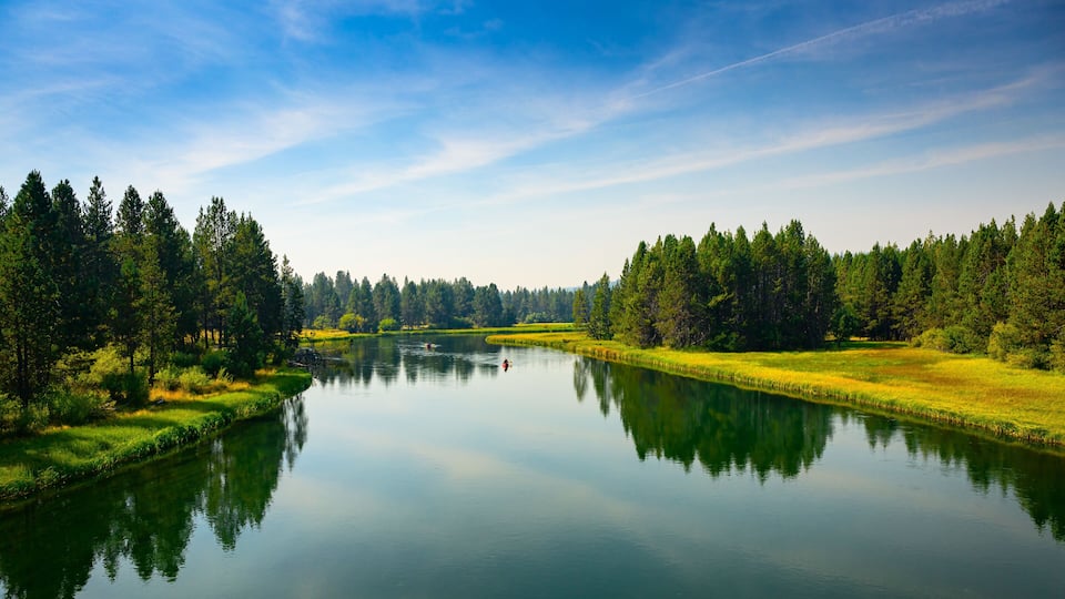 2024-09-10 THE DESCHUTES RIVER WITH A BEAUTIFUL REFLECTION IN THE WATER AND A GRASS AND TREE LINED SHORE IN SUNRIVER OREGON