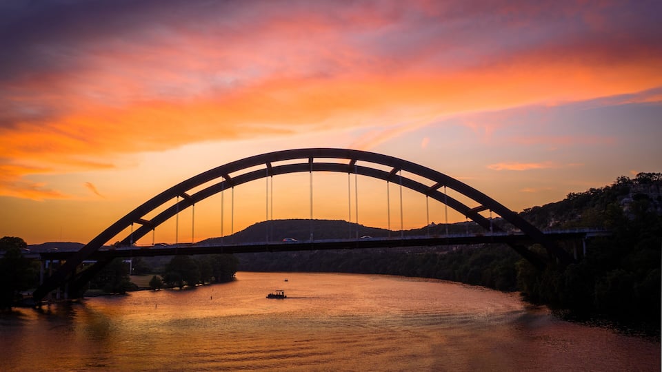 A bridge over a river at sunset with a boat in the water.