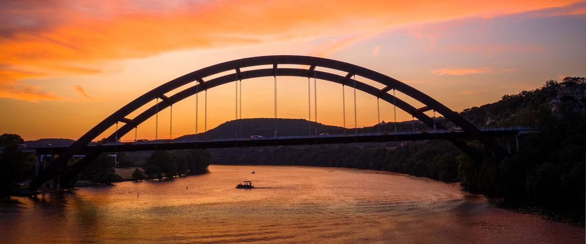 A bridge over a river at sunset with a boat in the water.