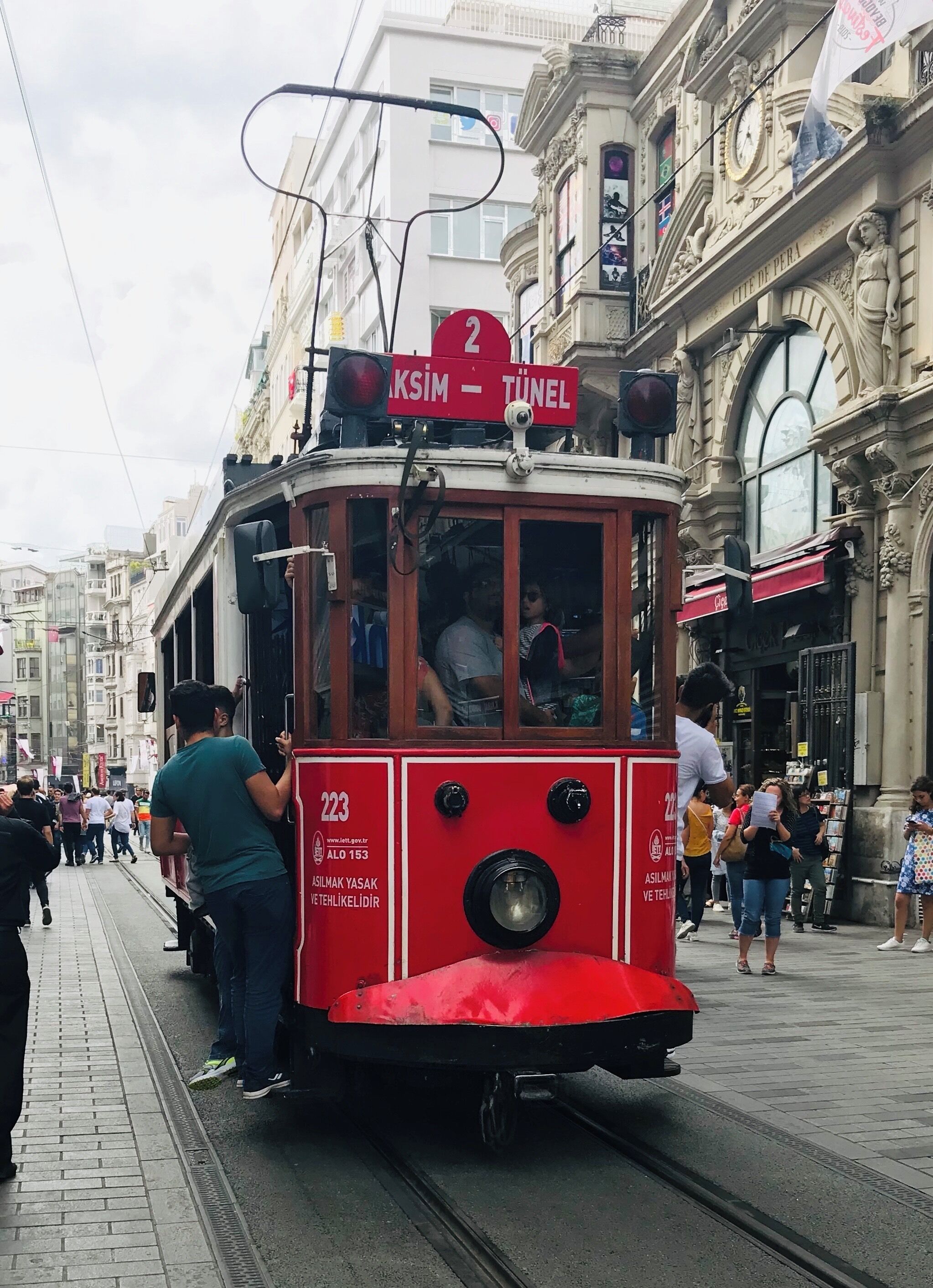 A red tram with a sign reading "KSIIM - TUNEL" on a street with pedestrians and historic buildings.