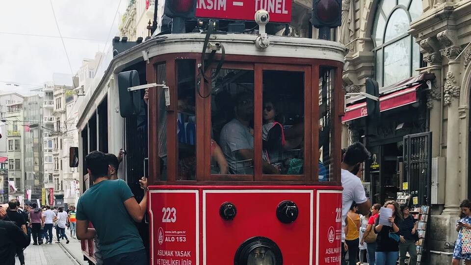 A red tram with a sign reading "KSIIM - TUNEL" on a street with pedestrians and historic buildings.