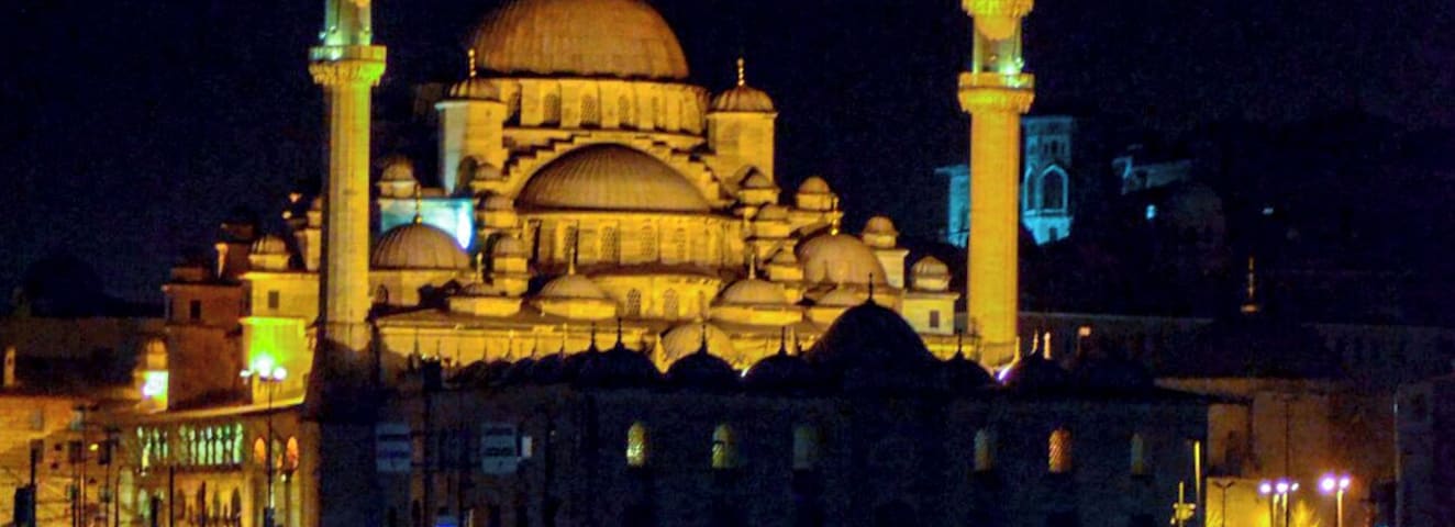 Uma mesquita com duas minaretes e uma cúpula grande, iluminada à noite.