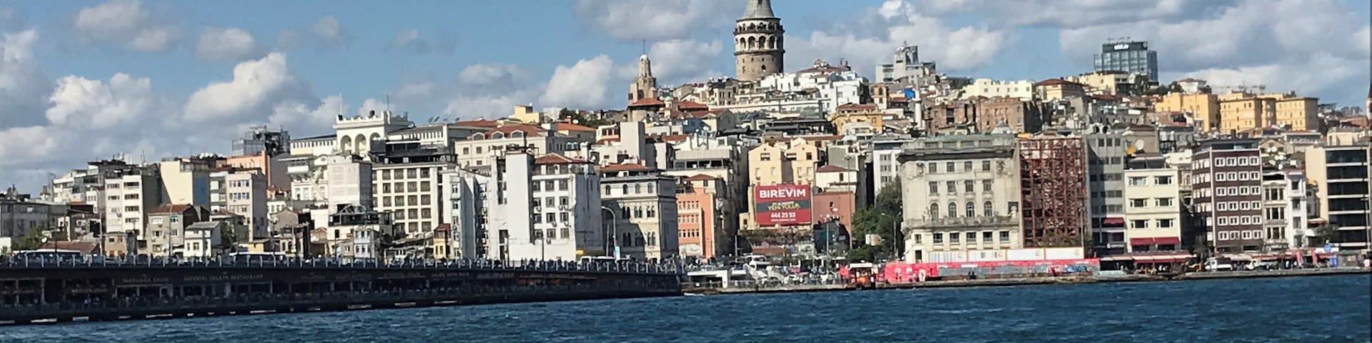 Un paisaje urbano costero con una torre destacada y un animado paseo marítimo.