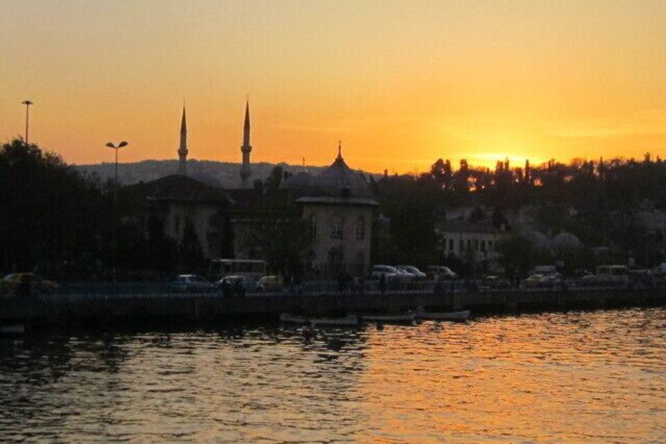 Un coucher de soleil sur une ville, avec une rivière, des bâtiments et deux minarets imposants.