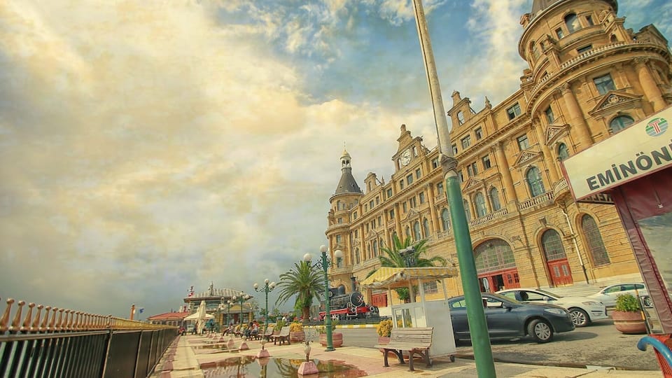 A grand building with a clock tower, a fountain, and parked cars.