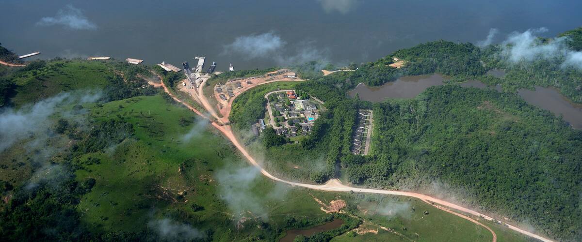An aerial view of a coastal area with a large body of water, a small island, and a complex of buildings near the shore.