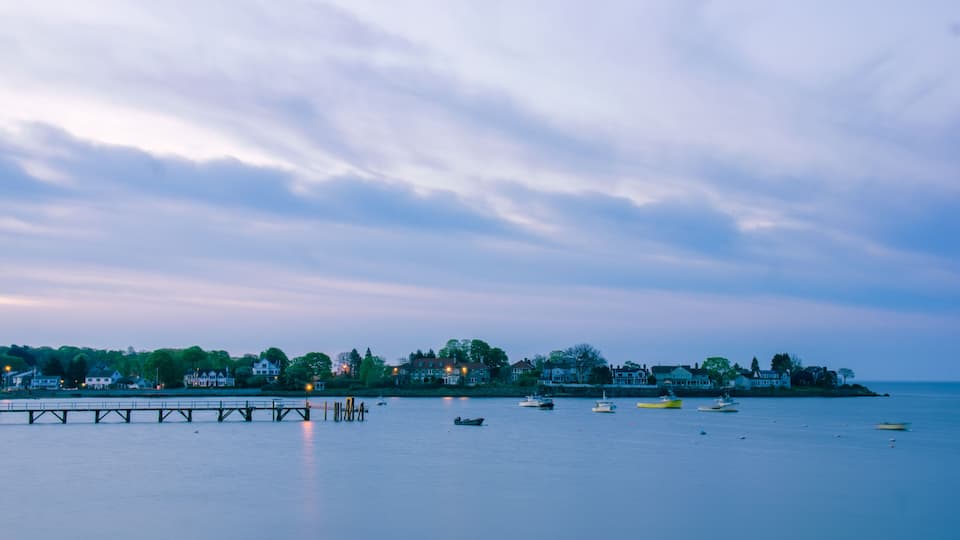 A calm waterfront with a pier extending into the water, surrounded by houses and boats.