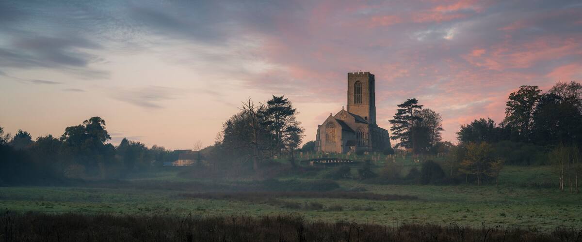 A church with a tall tower, surrounded by trees and a field.