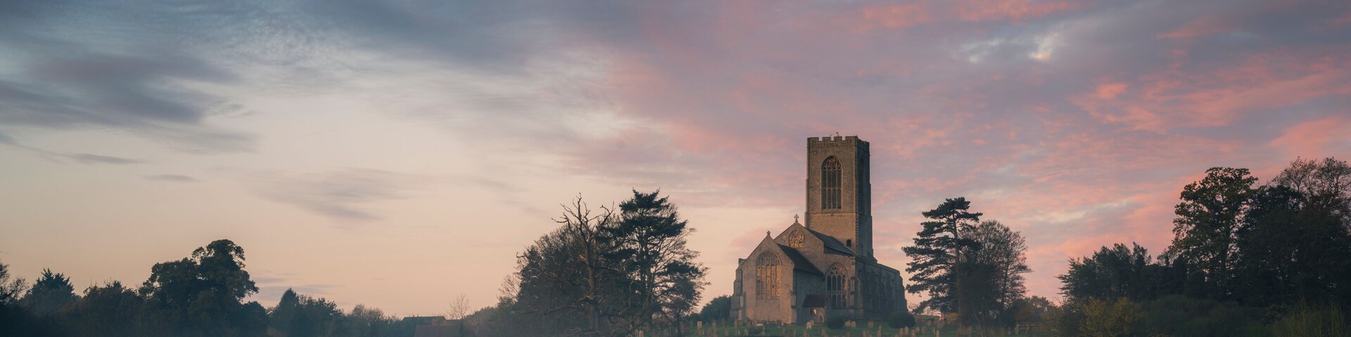 A church with a tall tower, surrounded by trees and a field.