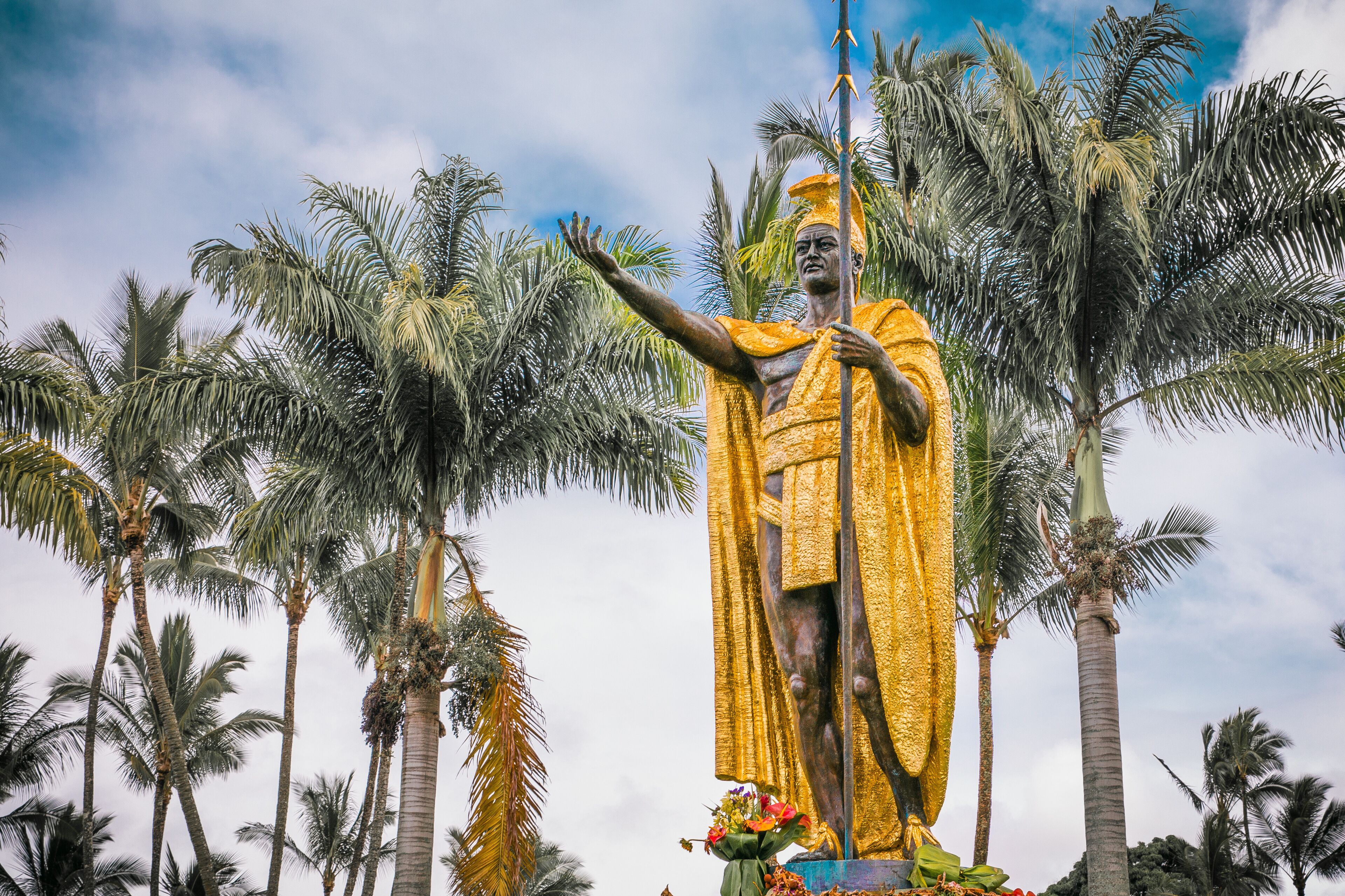 A large golden statue of a figure with outstretched arms, surrounded by palm trees and a clear sky.