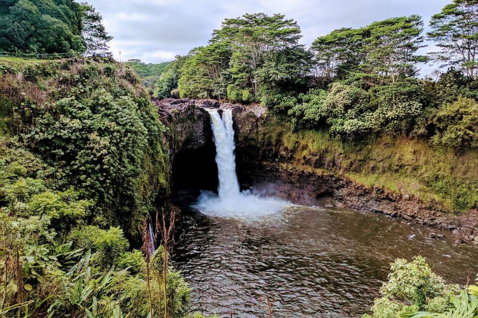 Una cascada que es verteig a un riu envoltat de verdura exuberanta.