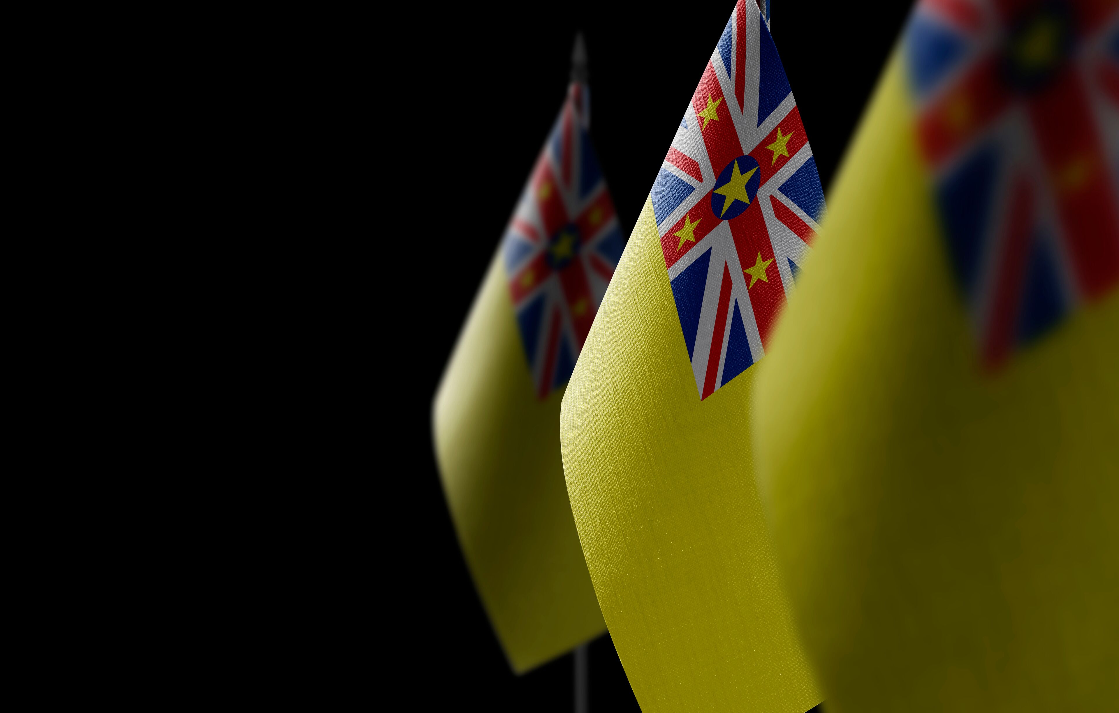 Small national flags of the Niue on a black background