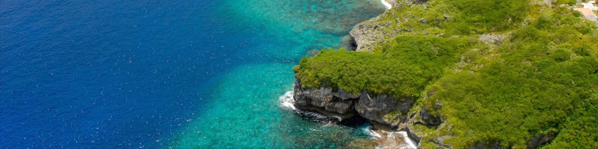 A coastal landscape with clear blue waters, rocky cliffs, and lush greenery.