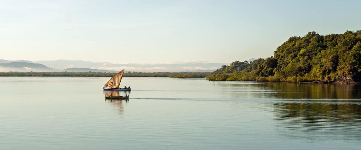 A calm lake with a sailboat in the center, surrounded by mountains and a forested island.