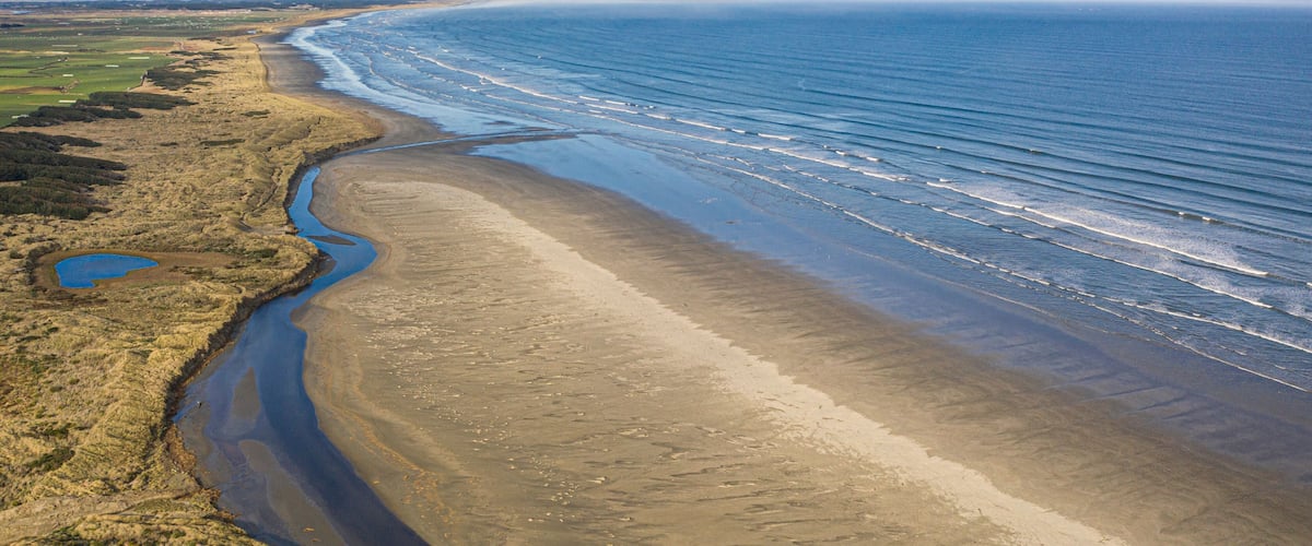 A coastal landscape with a sandy beach, a river flowing into the sea, and distant landforms.