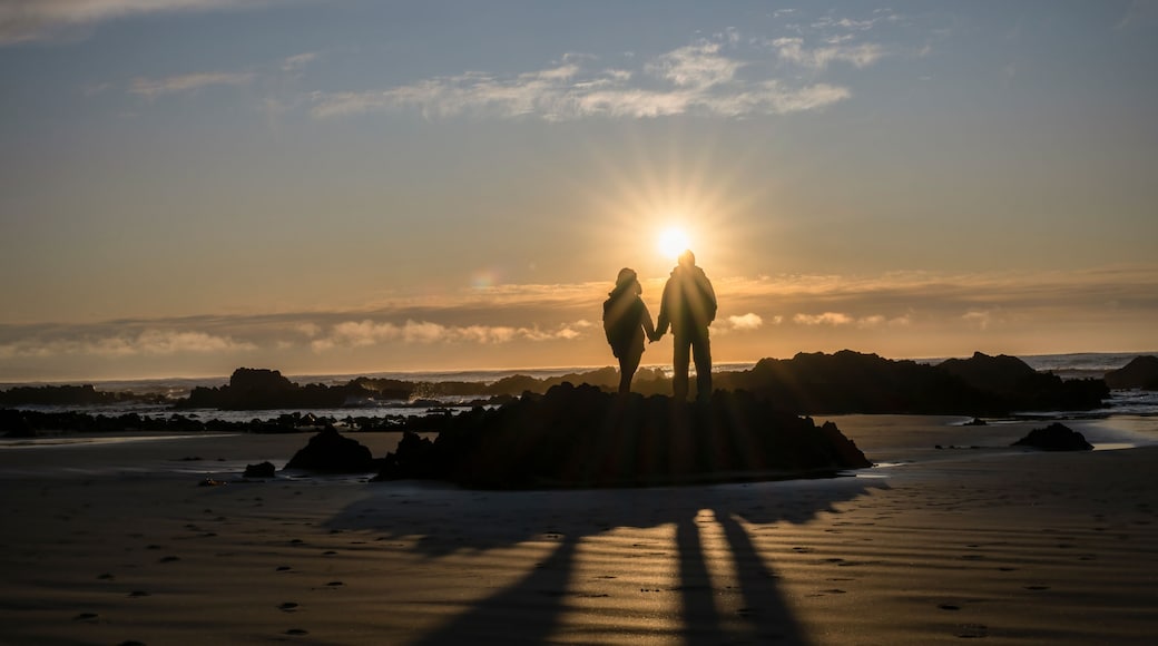 Couple holding hands, watching the sunrise at a rocky beach. Catlins, South Island.