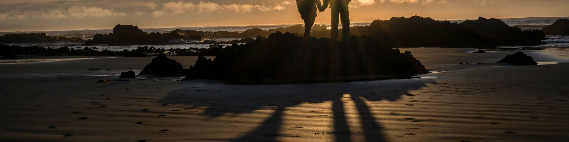 Couple holding hands, watching the sunrise at a rocky beach. Catlins, South Island.